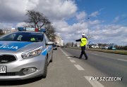 fotografia przedstawiająca policyjny oznakowany radiowóz marki kia oraz policjanta zatrzymującego pojazd do kontroli drogowej