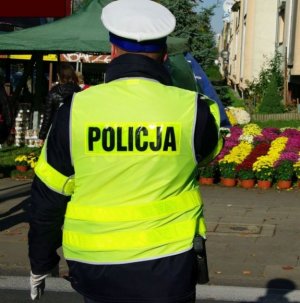 policjant ruchu drogowego w kamizelce odblaskowej oraz białej czapce. w tle widoczne są chryzantemy